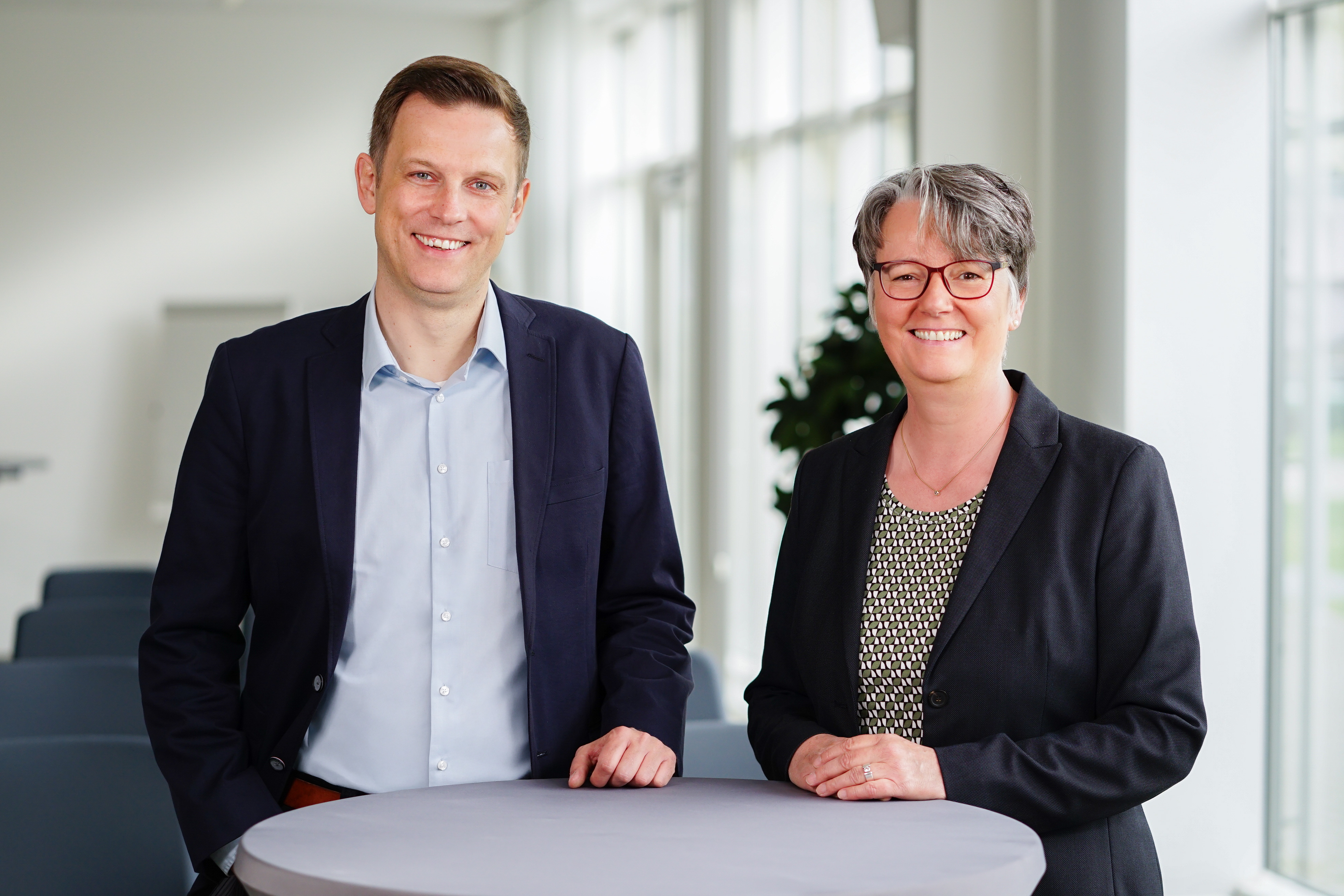 Referatsleiter und Referatsleiterin am Stehtisch schauen in die Kamera