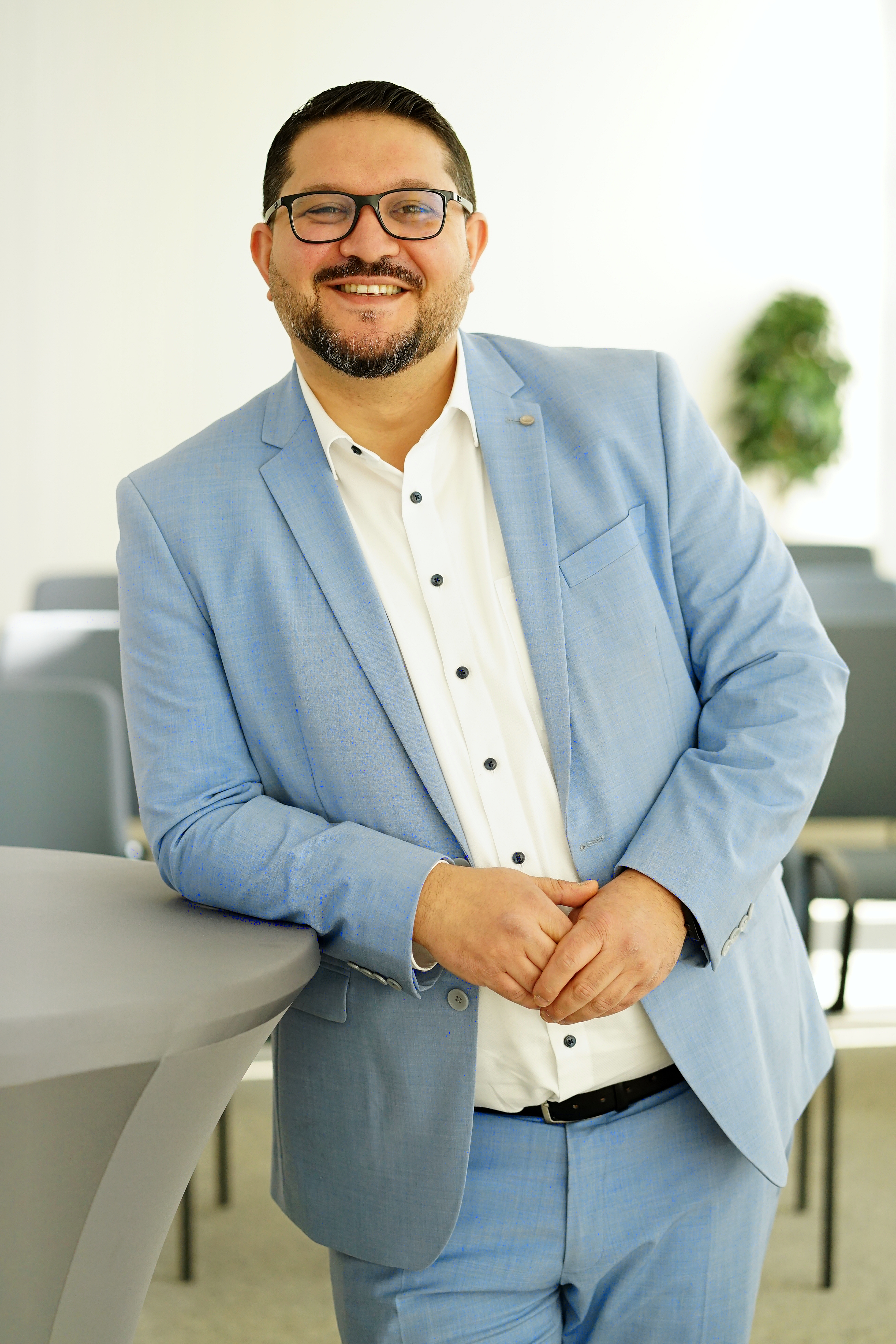 Mann im Anzug lehnt am Stehtisch und schaut in die Kamera.