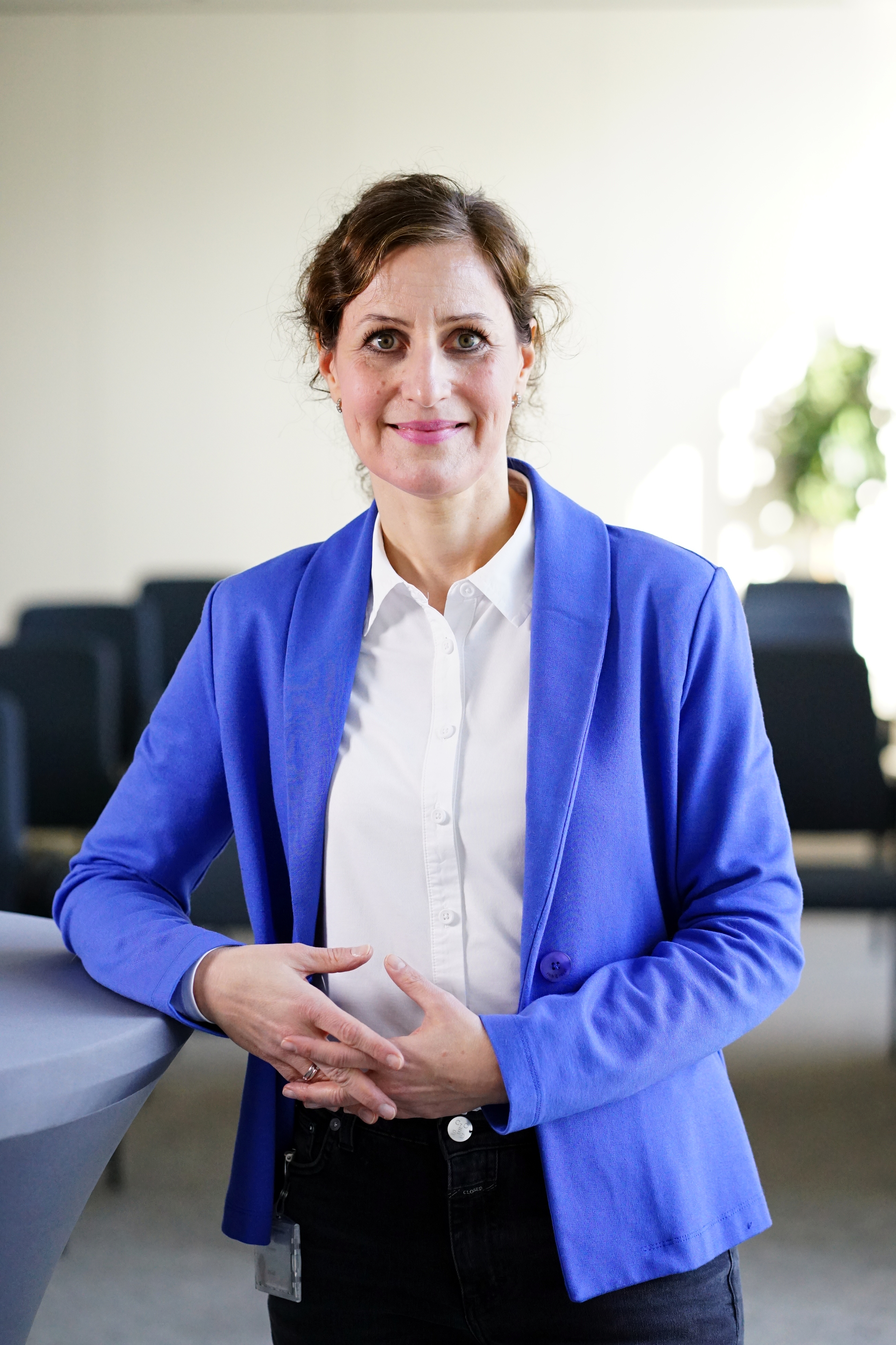 Dame im Blazer steht am Stehtisch und schaut in die Kamera.
