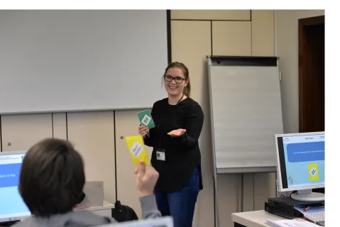 Corinna Pott ist in einem Schulungsraum zu sehen. Vorne im Bild sieht man einen Schulungsteilnehmer von hinten, er sitzt an einem Computer.
