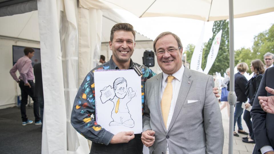 Karikaturist übergibt die Zeichnung an Ministerpräsident Armin Laschet