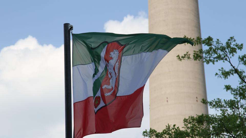 Die NRW-Flagge weht, im Hintergrund ist ein ein Teil des Reinturms zu sehen. 