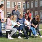 Eine Gruppe von Studentinnen und Studenten sitzen auf einer Bank unterhalten sich, im Hintergrund ist das Schloss Nordkirchen zu sehen.